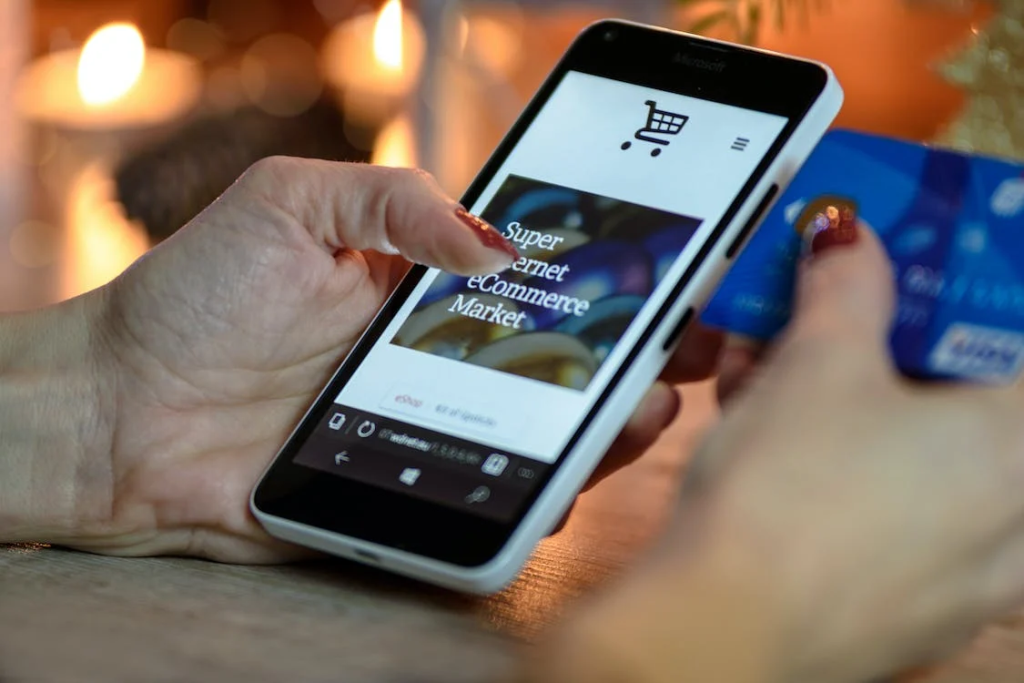 uma mão feminina segura um smartphone e um cartão de crédito, parece estar realizando o cadastro para efetuar uma compra online.